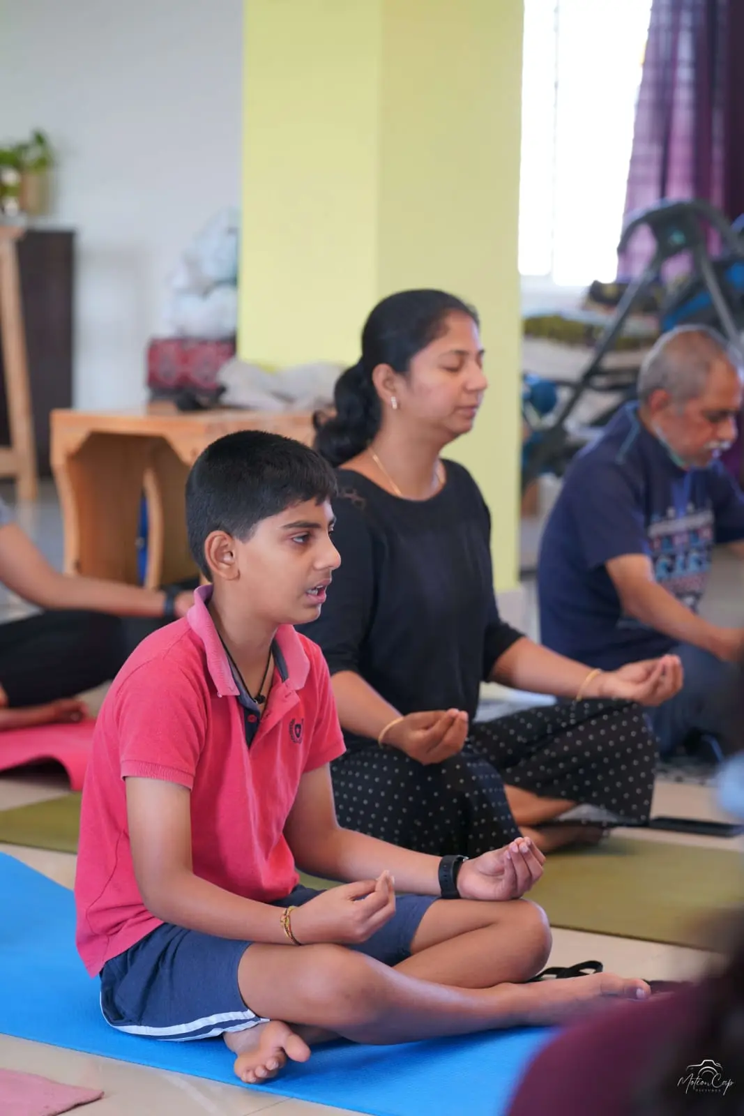 A young student seated in meditation on a blue yoga mat