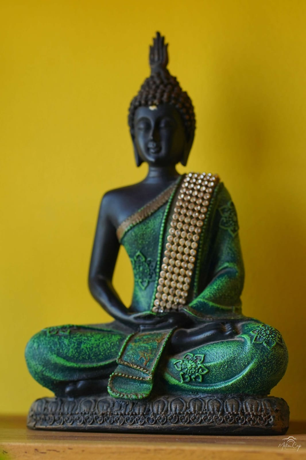 A green and bronze seated Buddha statue against a warm yellow wall
