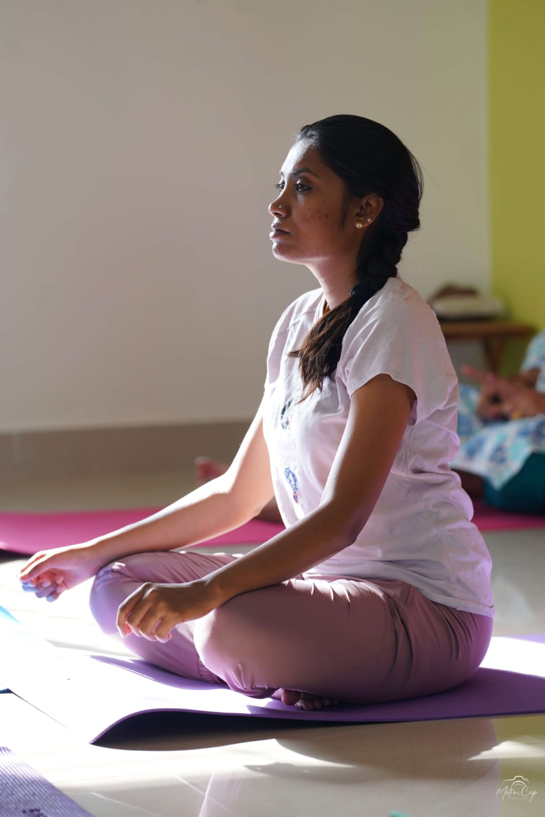 A woman seated in meditation as sunlight falls across the studio floor