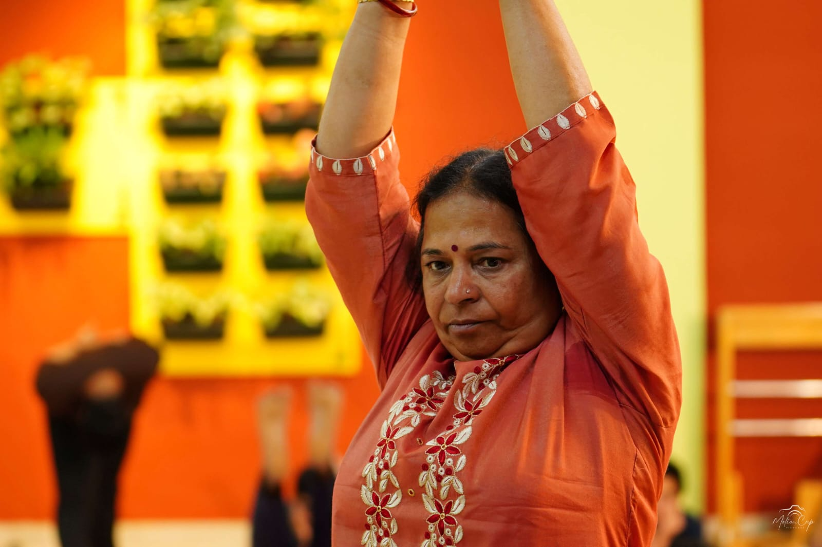 A student stretching both arms upward beneath a wall of green planters