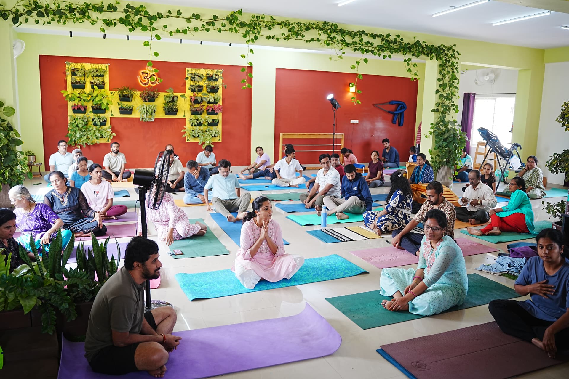 A large group of students seated on yoga mats inside the Guru Paduka studio