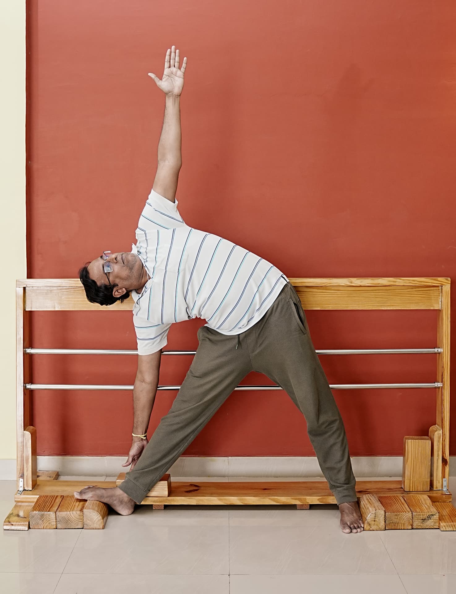 A practitioner in triangle pose beside a wooden wall rope frame
